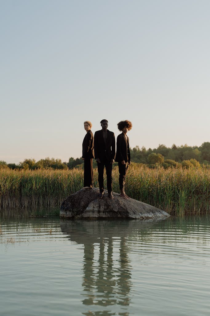 Three models elegantly pose atop a rock in a scenic meadow, surrounded by nature.